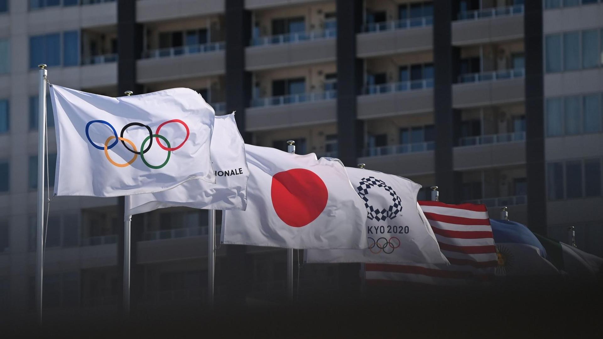 Die Olympische Flagge weht neben der japanischen und weiteren nationalen Flaggen im Wind.