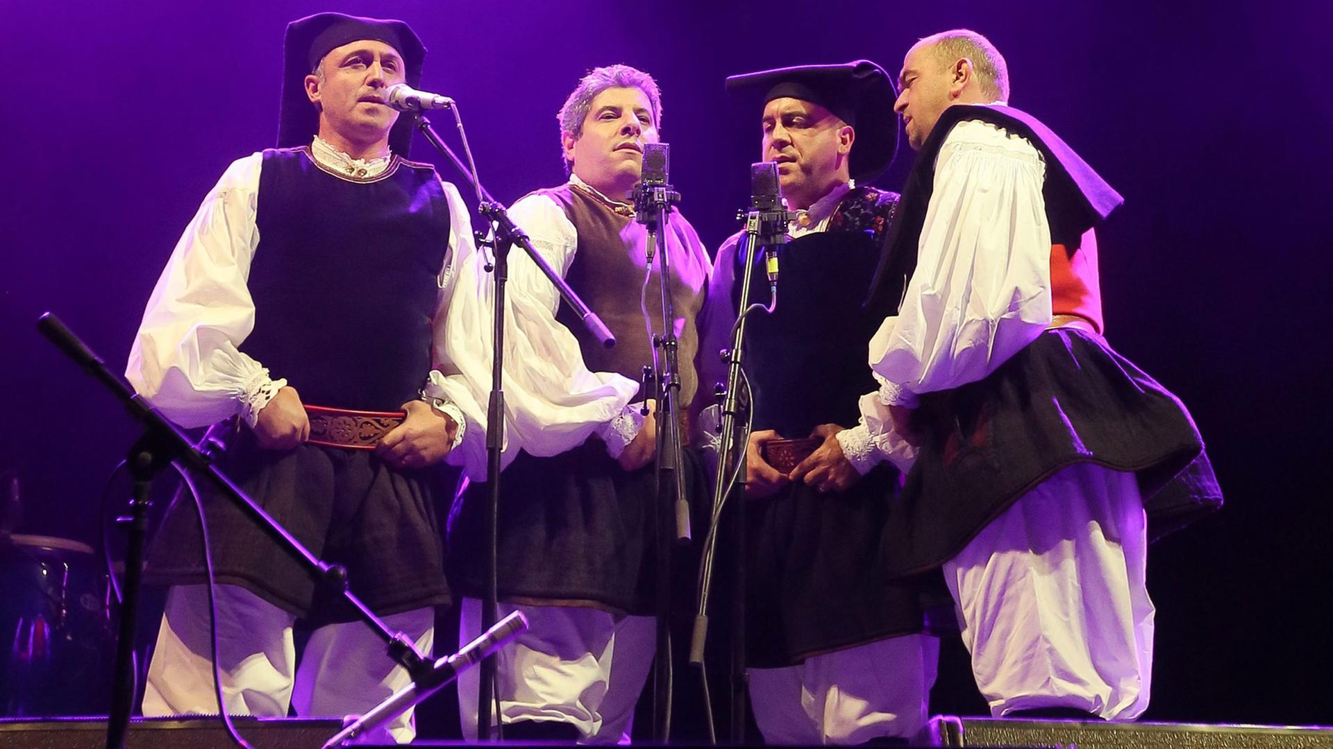 Das sardische Vokalquartett Tenores di Bitti "Mialinu Pira" steht in traditioneller Kleidung auf einer Bühne. Das sardische Vokalquartett Tenores di Bitti "Mialinu Pira" steht in traditioneller Kleidung auf einer Bühne.