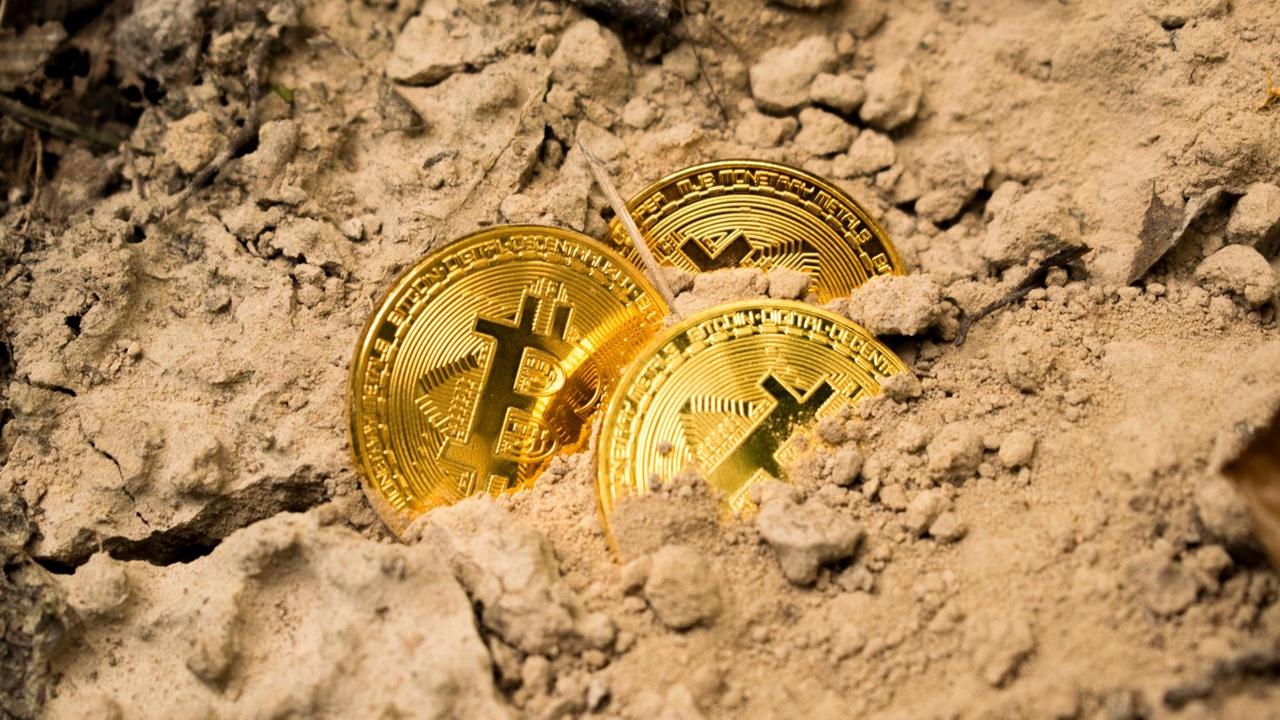 Drei golden schimmernde Bitcoin-Münzen liegen, halb vergraben, im Sand. Drei golden schimmernde Bitcoin-Münzen liegen, halb vergraben, im Sand.