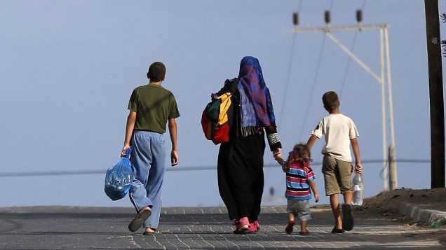 Vier Menschen, darunter zwei Kinder, gehen mit gepackten StraÃen auf einer StraÃe.