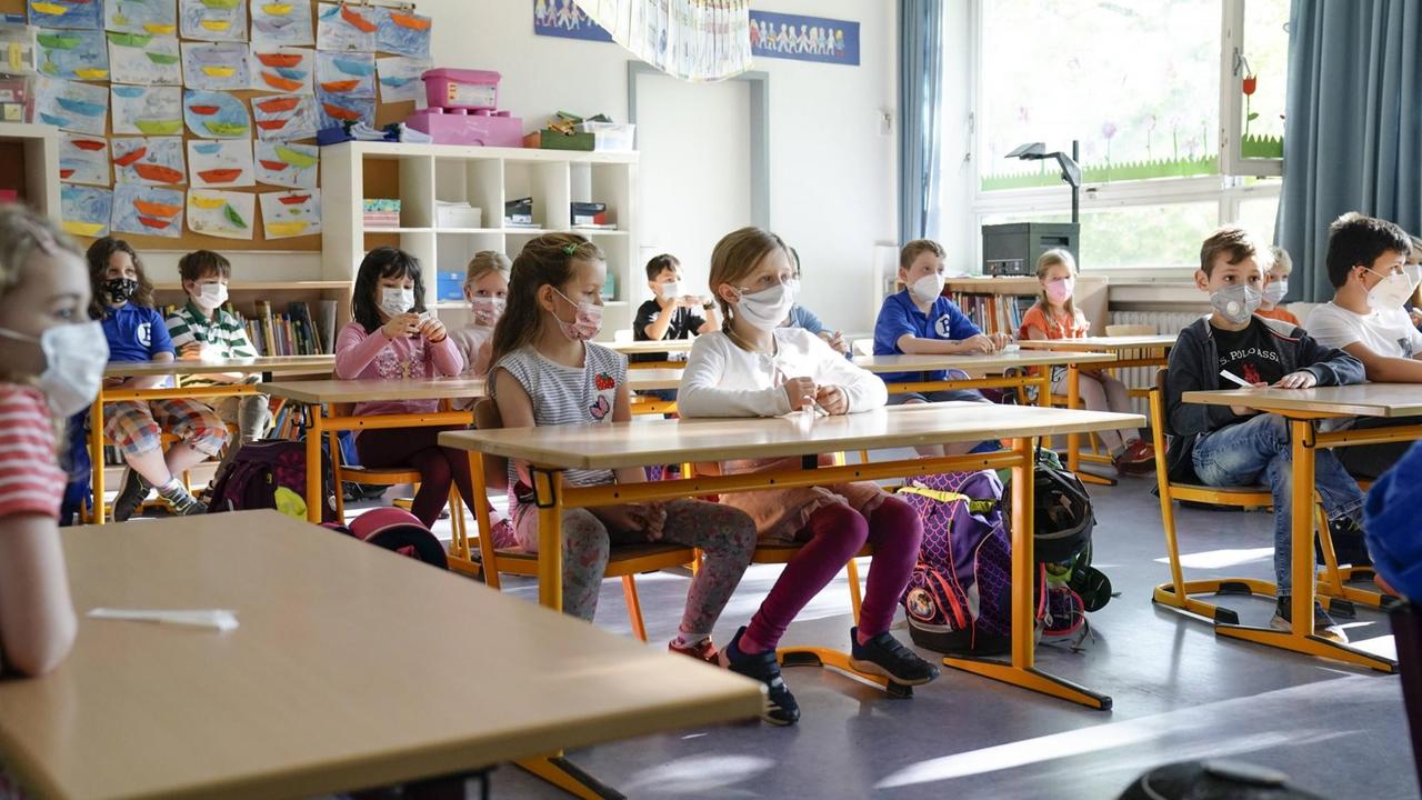 Grundschüler zu zweit an ihren Tischen, mit Mundschutz Grundschüler zu zweit an ihren Tischen, mit Mundschutz