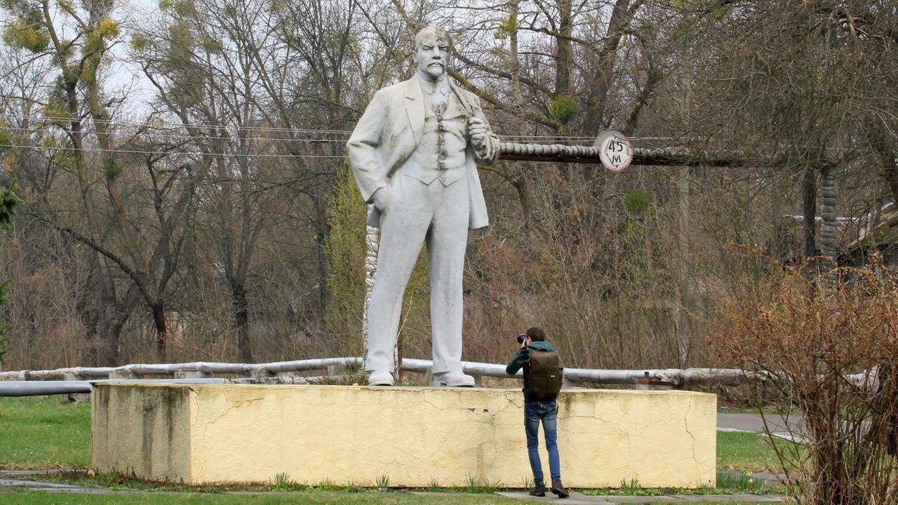 Ein Man macht ein Foto von einer Lenin-Statue, die umgeben von Büschen in der Tschernobyl-Schutzzone steht.