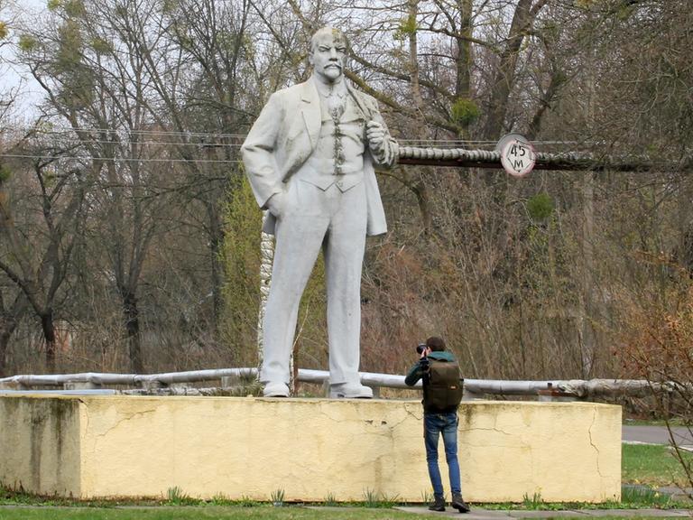 Ein Man macht ein Foto von einer Lenin-Statue, die umgeben von Büschen in der Tschernobyl-Schutzzone steht.