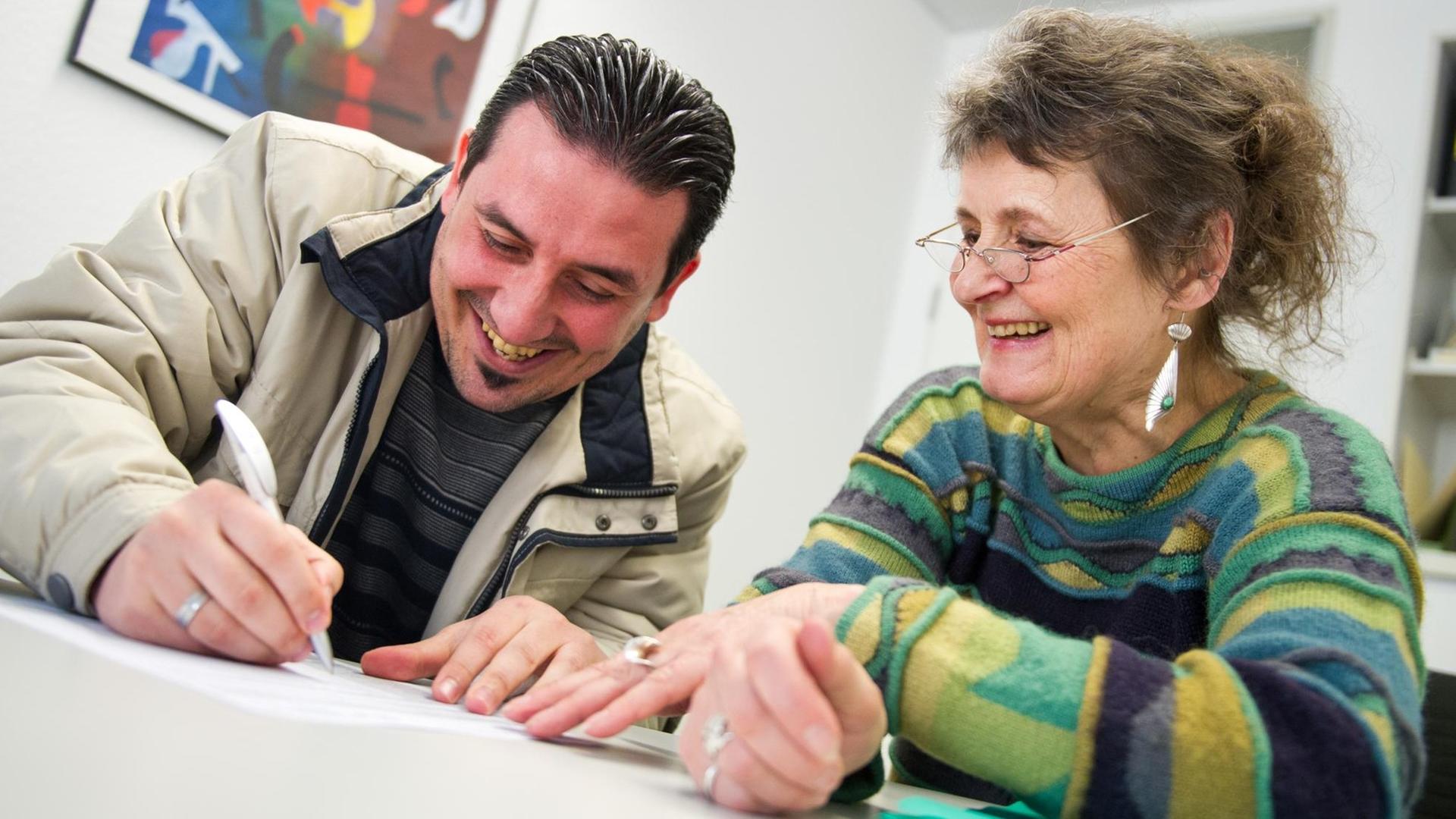 Der syrische Flüchtling Obayda Daoud (l) sitzt am 20.03.2015 in einem Büro der Nassauischen Wohnungsgesellschaft in Offenbach am Main (Hessen) neben Flüchtlingspatin Friedegard Enders und füllt zusammen mit ihr Formulare für den Erhalt einer Wohnung aus. Der syrische Flüchtling Obayda Daoud (l) sitzt am 20.03.2015 in einem Büro der Nassauischen Wohnungsgesellschaft in Offenbach am Main (Hessen) neben Flüchtlingspatin Friedegard Enders und füllt zusammen mit ihr Formulare für den Erhalt einer Wohnung aus.