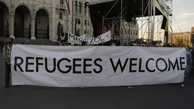 Eine Gruppe von Aktivisten protestiert gegen die Politik ihrer ungarischen Regierung und hält ein Schild, auf dem steht: Refugees welcome, Flüchtlinge willkommen.