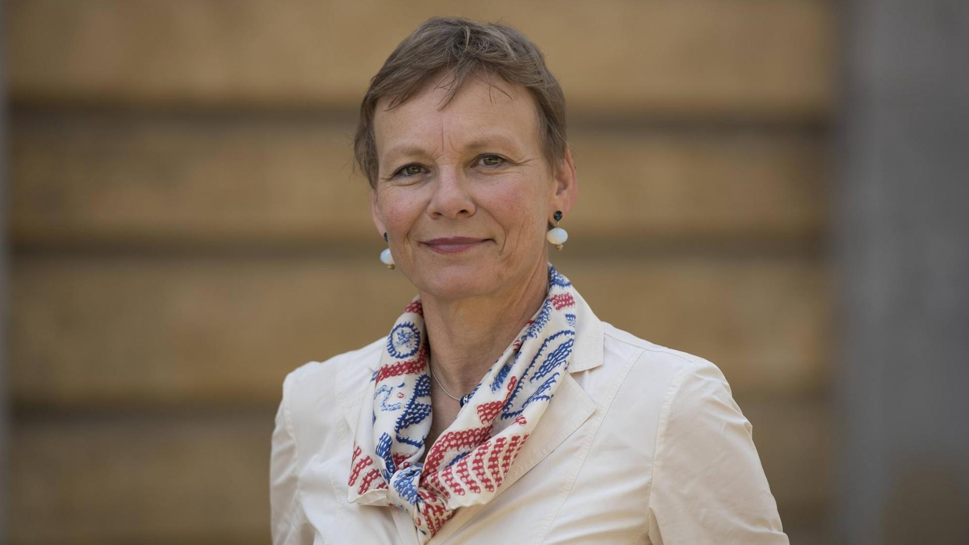 Sabine Kunst, mit kurzen Haaren steht in heller Jacke vor einem hellbraunen Hintergrund und lächelt in die Kamera. Sabine Kunst, mit kurzen Haaren steht in heller Jacke vor einem hellbraunen Hintergrund und lächelt in die Kamera.
