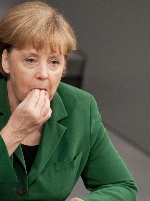 Bundeskanzlerin Angela Merkel (CDU) sitzt am 25.10.2012 in Berlin im Plenarsaal des Bundestages und führt die rechte Hand an den Mund. Der Bundestag beschäftigt sich in seiner Sitzung unter anderem mit den Themen Rentenbeitragssatz, Praxisgebühr, Steuerabkommen mit der Schweiz, Betreuungsgeld und der Höchstgrenze für Minijobs. Foto: Robert Schlesinger/dpa