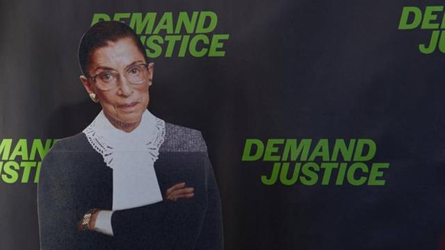 Die ehemalige Richterin des Supreme Courts der USA, Ruth Bader Ginsburg, als Fotoplakat-Figur vor einer schwarzen Wand, auf der wiederholt in grellgrüner Schrift "Demand Justice" - "Fordert Gerechtigkeit" steht.