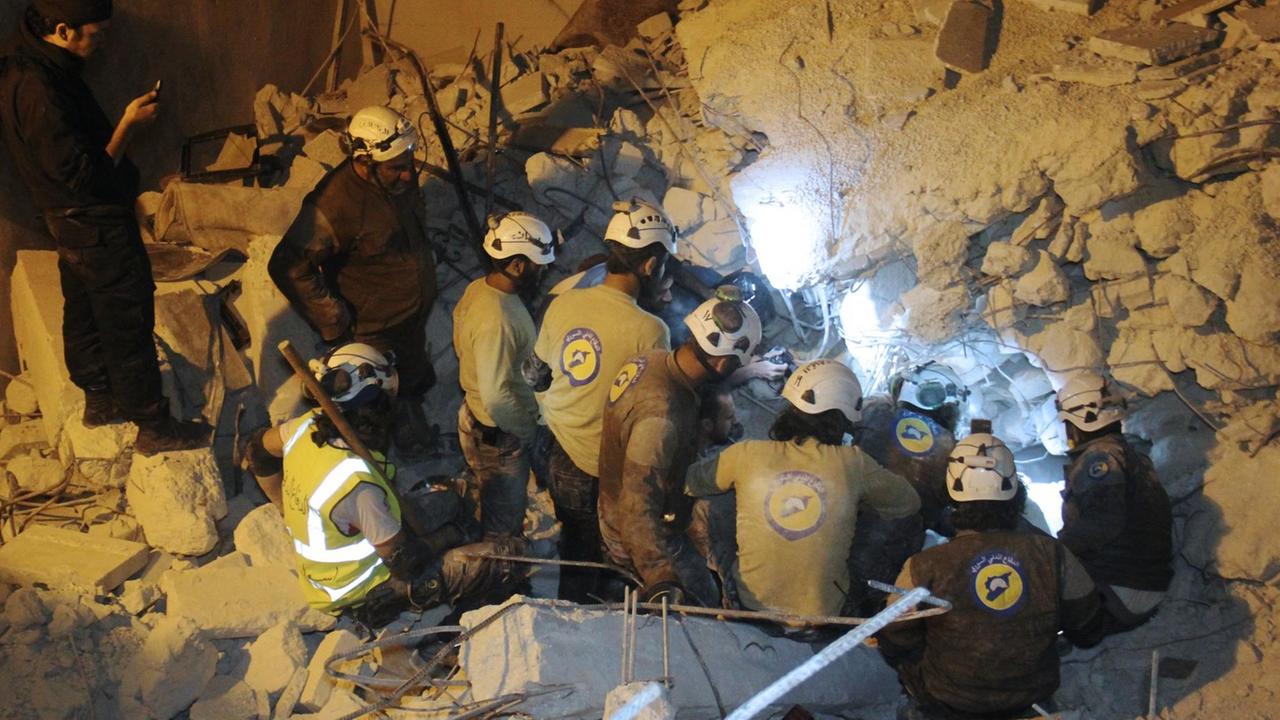 Helfer der Weißhelme knien vor einem Schutthaufen in Syrien bei einem Rettungsversuch Helfer der Weißhelme knien vor einem Schutthaufen in Syrien bei einem Rettungsversuch