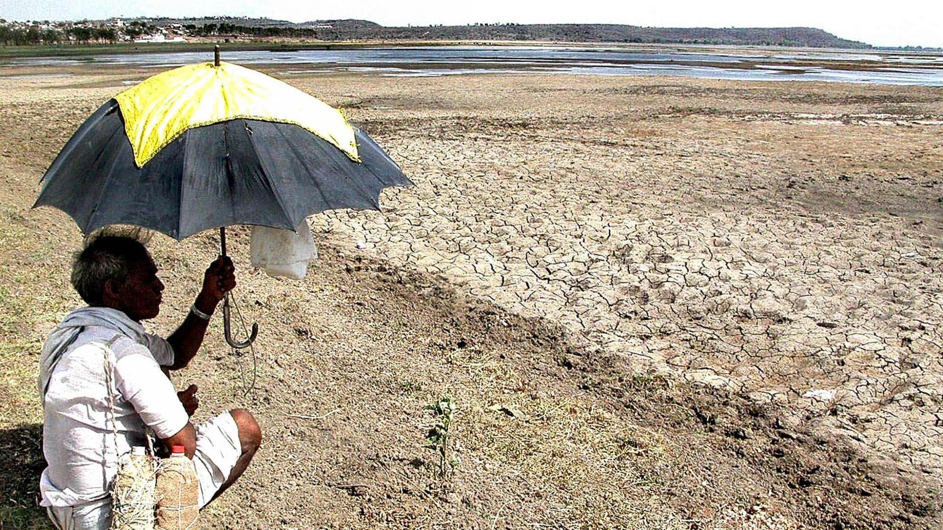 Ein Mann sitzt mit einem Sonnenschirm in der Hand am Ufer eines fast ausgetrockneten Sees im indischen Bhopal Ein Mann sitzt mit einem Sonnenschirm in der Hand am Ufer eines fast ausgetrockneten Sees im indischen Bhopal