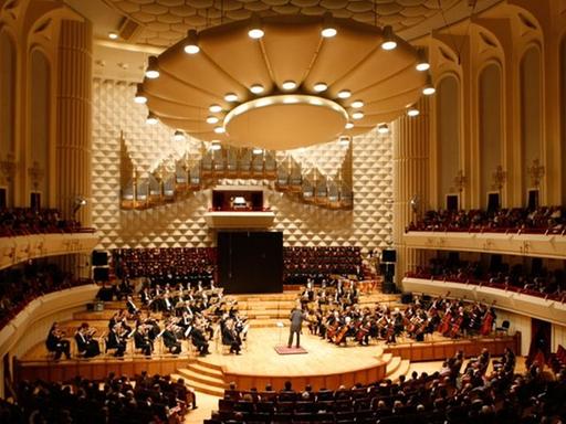 Ein großer Konzertsaal, auf der Bühne steht das Orchester.