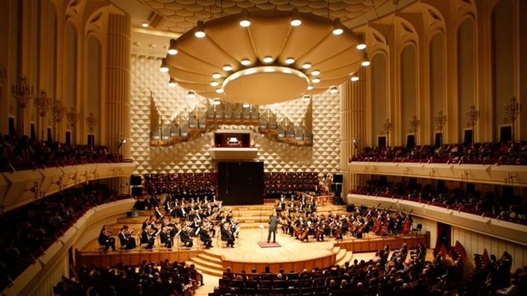 Ein großer Konzertsaal, auf der Bühne steht das Orchester.