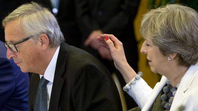 Die britische Premierministerin Theresa May (re.) setzt an, um EU-Kommissionspräsident Jean-Claude Juncker neben sich die Hand auf den Rücken zu legen.