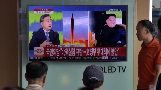 Menschen vor einem Fernsehgerät, auf dem über ein Raketenstart sowie der nordkoreanische Machthaber Kim Jong-Un gezeigt wird.