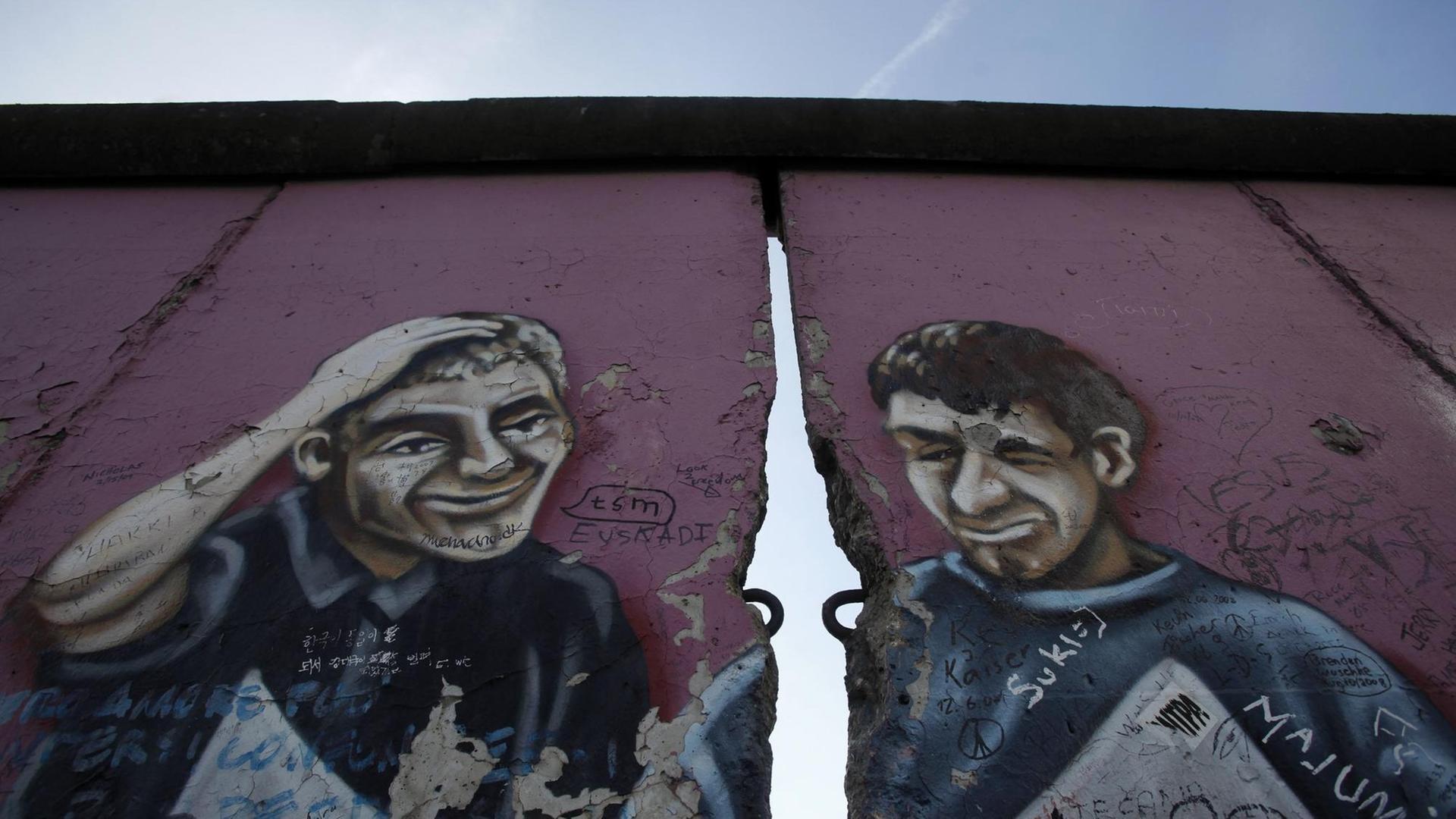 Ein ehemaliger Teil der East Side Gallery in Berlin zeigt ein Graffiti mit zwei Männern, getrennt durch einen Riss in der Mauer. Ein ehemaliger Teil der East Side Gallery in Berlin zeigt ein Graffiti mit zwei Männern, getrennt durch einen Riss in der Mauer.