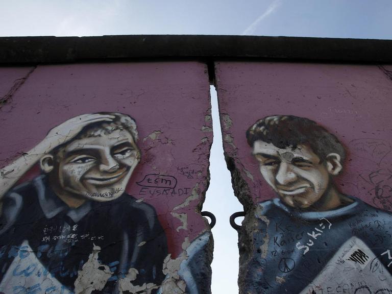 Ein ehemaliger Teil der East Side Gallery in Berlin zeigt ein Graffiti mit zwei Männern, getrennt durch einen Riss in der Mauer.