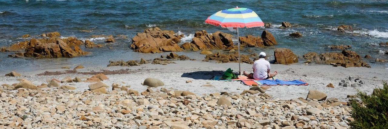 Ein Mann hat sich im Juni 2019 unter einem Sonnenschirm an einen Strand auf der italienischen Insel Sardinien gesetzt.