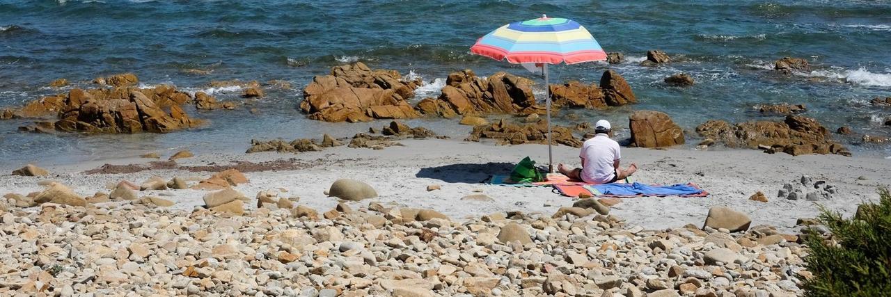 Ein Mann hat sich im Juni 2019 unter einem Sonnenschirm an einen Strand auf der italienischen Insel Sardinien gesetzt. Ein Mann hat sich im Juni 2019 unter einem Sonnenschirm an einen Strand auf der italienischen Insel Sardinien gesetzt.