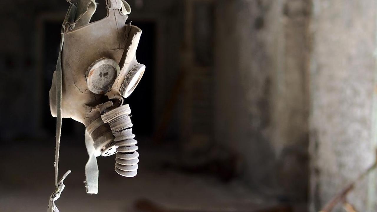 Eine Gasmaske hängt in einem Gang eines zerstörten Gebäudes von der Decke.