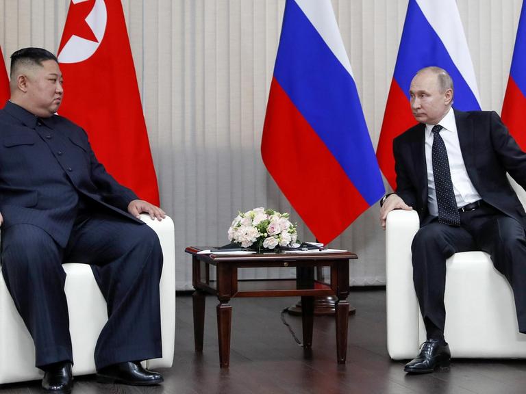 Nordkoreas Machhthaber Kim trifft Russlands Präsidenten Putin. Die beiden sitzen in Ledersesseln vor den Flaggen ihrer Länder und sehen sich an.