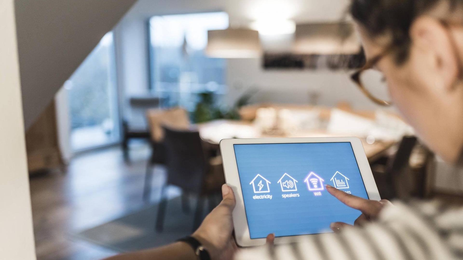 Eine Frau steuert via Tablet verschiedene Smart Home-Funktionen an. Eine Frau steuert via Tablet verschiedene Smart Home-Funktionen an.