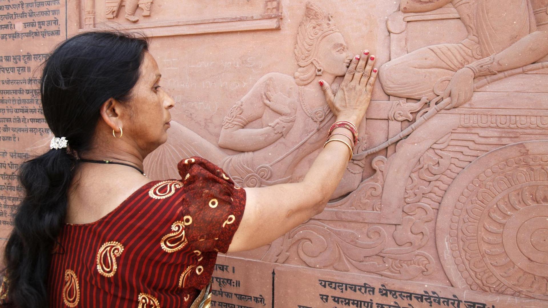 Eine Inderin berührt mit ihren Händen das Relief der in den Hindutempel eingemeiselten Bhagavadgita. Eine Inderin berührt mit ihren Händen das Relief der in den Hindutempel eingemeiselten Bhagavadgita.