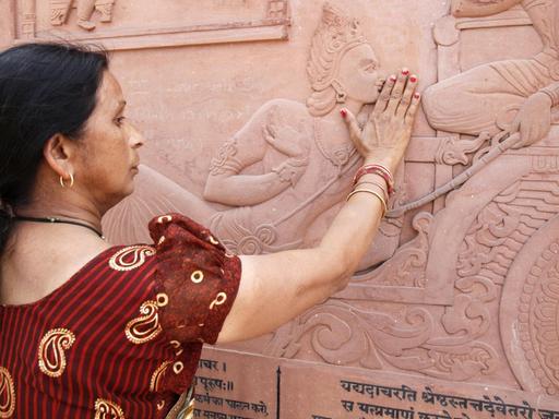 Eine Inderin berührt mit ihren Händen das Relief der in den Hindutempel eingemeiselten Bhagavadgita.