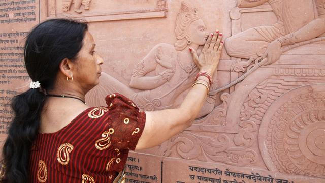 Eine Inderin berührt mit ihren Händen das Relief der in den Hindutempel eingemeiselten Bhagavadgita.