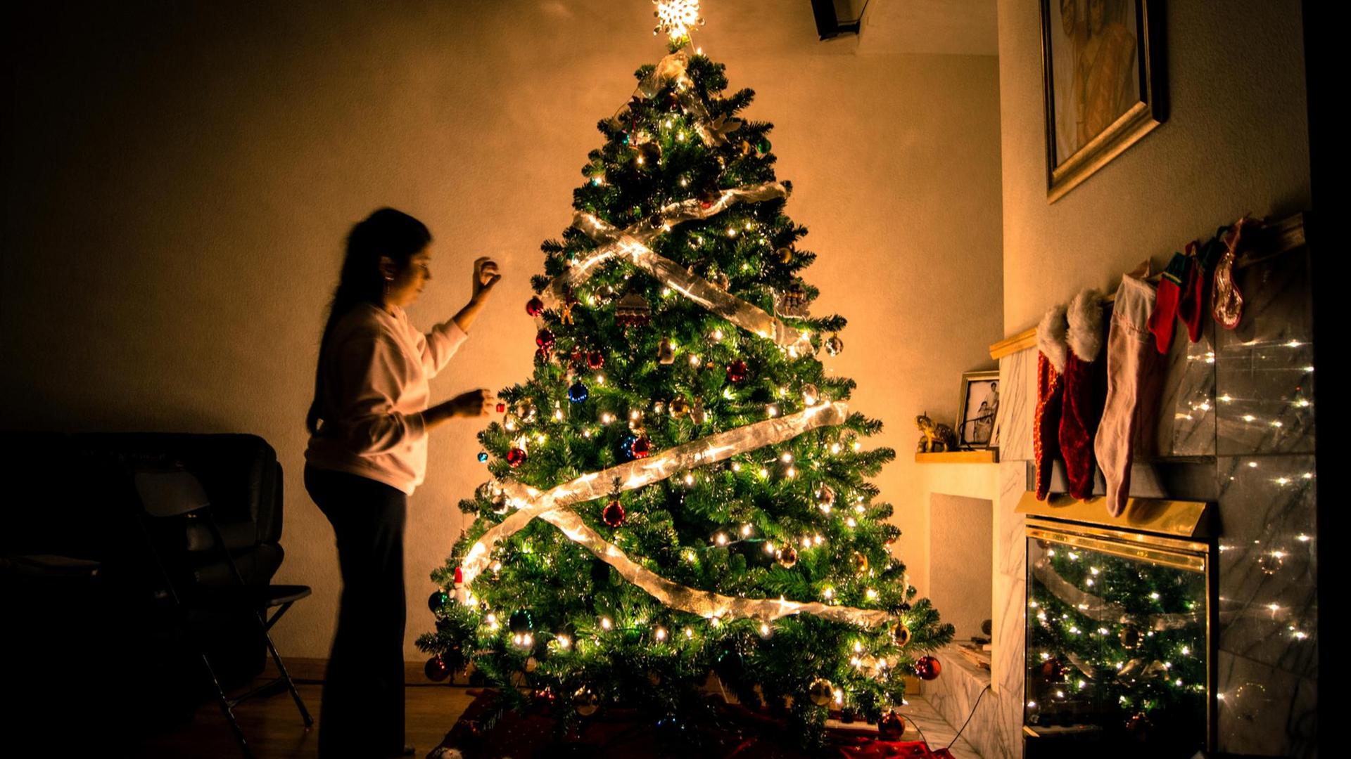 Eine Frau schmückt einen leuchtenden Weihnachtsbaum. Eine Frau schmückt einen leuchtenden Weihnachtsbaum.