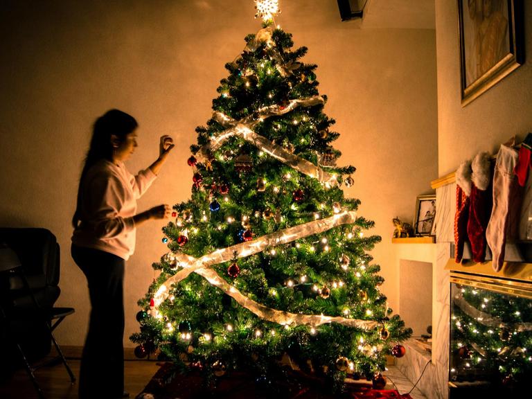 Eine Frau schmückt einen leuchtenden Weihnachtsbaum.