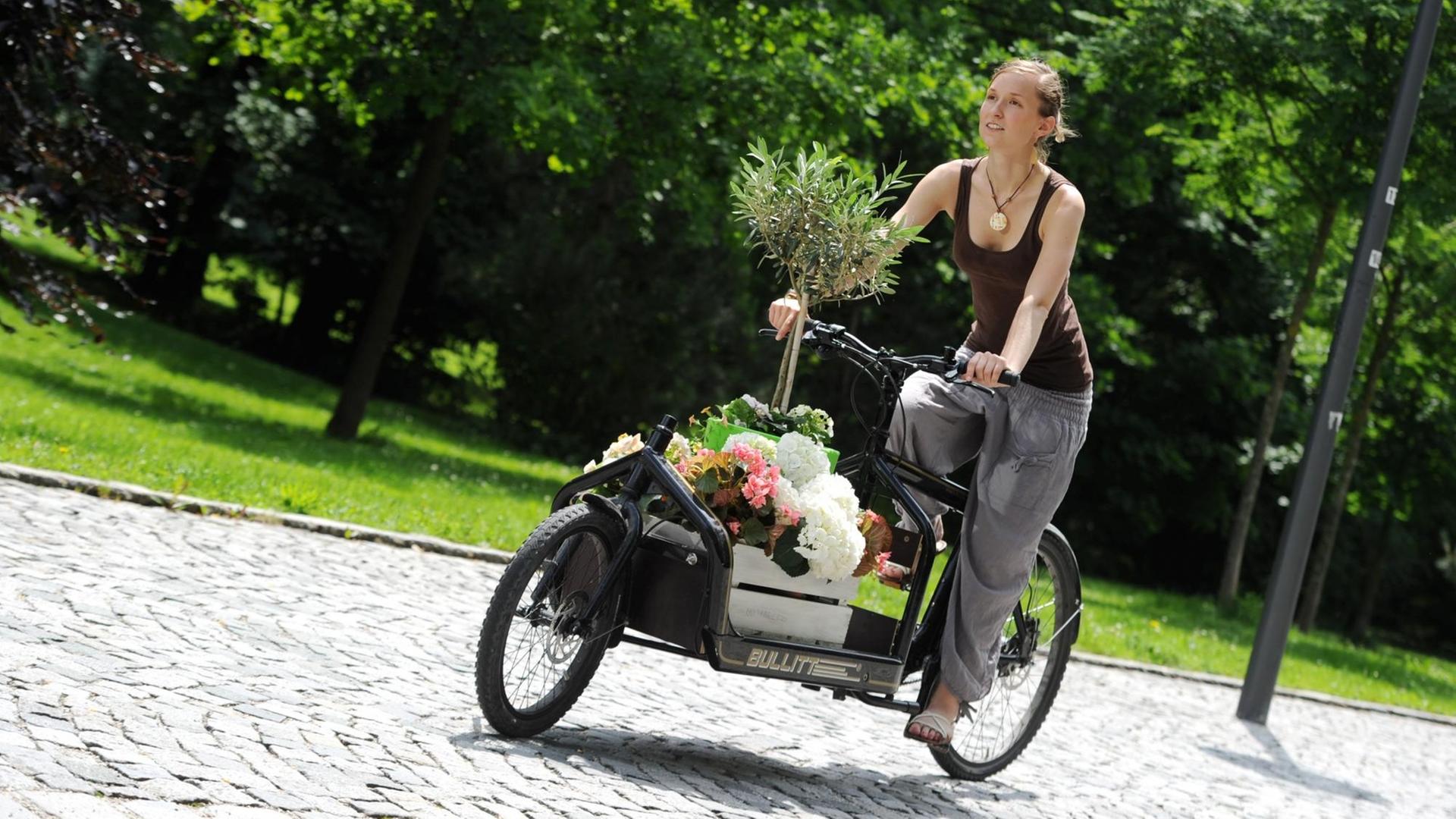Eine Frau fährt mit einem Transportrad, das mit Blumen beladen ist. Mit Denkfabrik-Stempel Eine Frau fährt mit einem Transportrad, das mit Blumen beladen ist. Mit Denkfabrik-Stempel