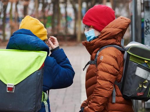 Zwei Schüler, die medizinische Masken tragen, kommen mit Schulranzen zum Eingang einer Grundschule im Berliner Bezirk Prenzlauer Berg.