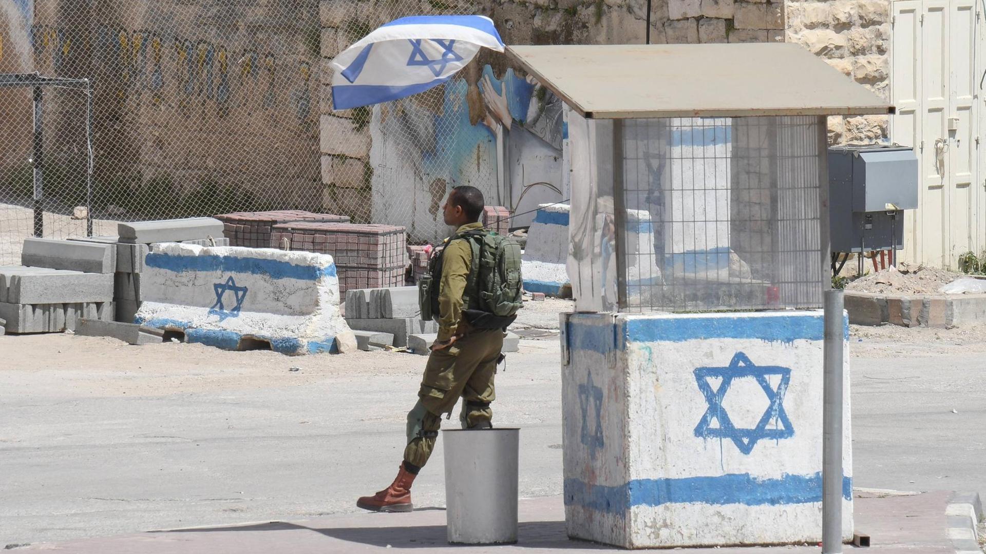 Israelische Kontrollstelle in Hebron im Westjordanland/Palaestina: Ein Israelischer Soldat in Uniform steht vor einem Wachhäuschen, das mit einer gemalten israelischen Flagge angestrichen ist.