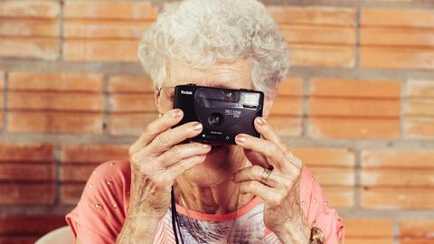 Eine ältere Dame guckt durch einen Fotoapparat.