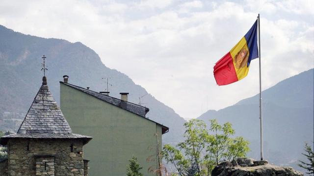 Die Nationalflagge von Andorra weht neben Häusern der Hauptstadt Andorra la Vella, im Hintergrund sind die Pyrenäen zu erkennen. Aufnahme vom 01.09.2005.