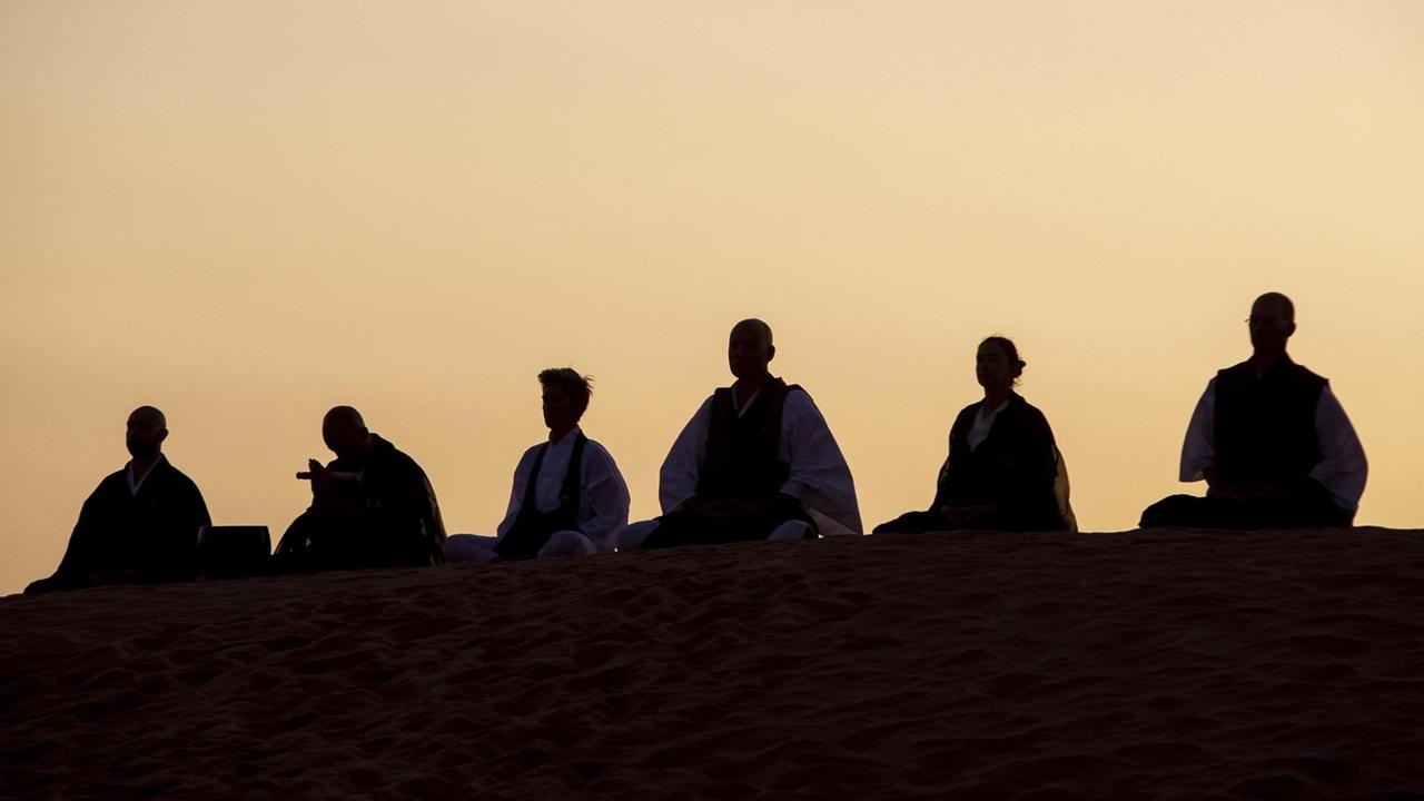 Silhouetten von sitzenden Menschen, die während der Dämmerung auf einer Düne meditieren. Silhouetten von sitzenden Menschen, die während der Dämmerung auf einer Düne meditieren.