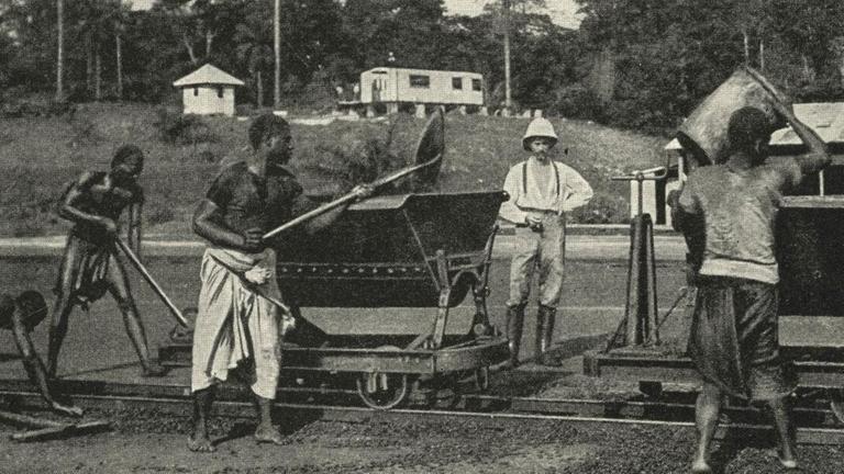 Unter Aufsicht eines deutschen Kolonisten verladen Arbeiter 1914 in Kamerun Kakaobohnen. Unter Aufsicht eines deutschen Kolonisten verladen Arbeiter 1914 in Kamerun Kakaobohnen.
