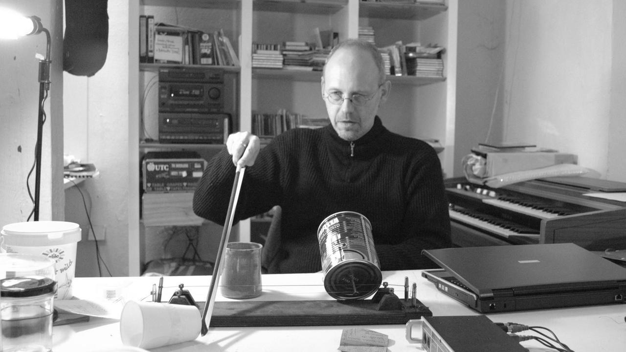 Am Tisch sitzend, streicht Christoph Ogiermann verschiedene Gegenstände mit dem Geigenbogen