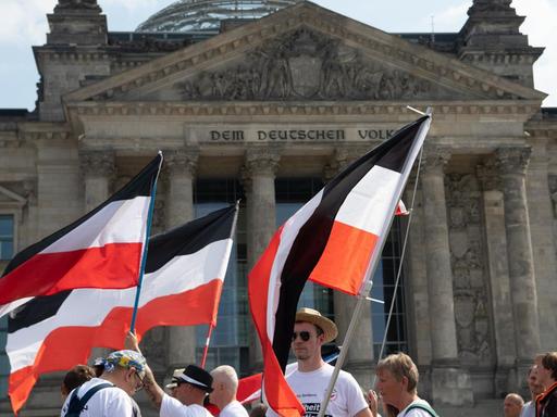 Mit ehemaligen Reichsfahnen stehen Demonstranten vor dem Reichstag.