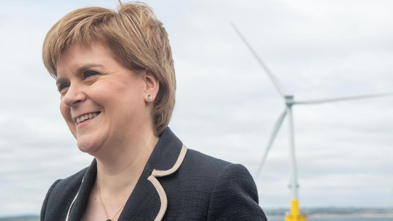 Schottlands Erste Ministerin Nicola Sturgeon vor blauem Himmel, im Hintergrund ist ein Windrad in der Nordsee zu sehen. Schottlands Erste Ministerin Nicola Sturgeon vor blauem Himmel, im Hintergrund ist ein Windrad in der Nordsee zu sehen.