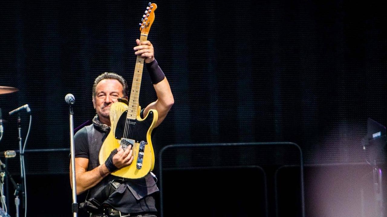 Bruce Sprungsteen mit The E Street Band auf der Bühne in Mailand: Er spielt seine Gitarre senktrecht, im Hintergrund ist sein Schlagzeuger zu sehen. Bruce Sprungsteen mit The E Street Band auf der Bühne in Mailand: Er spielt seine Gitarre senktrecht, im Hintergrund ist sein Schlagzeuger zu sehen.