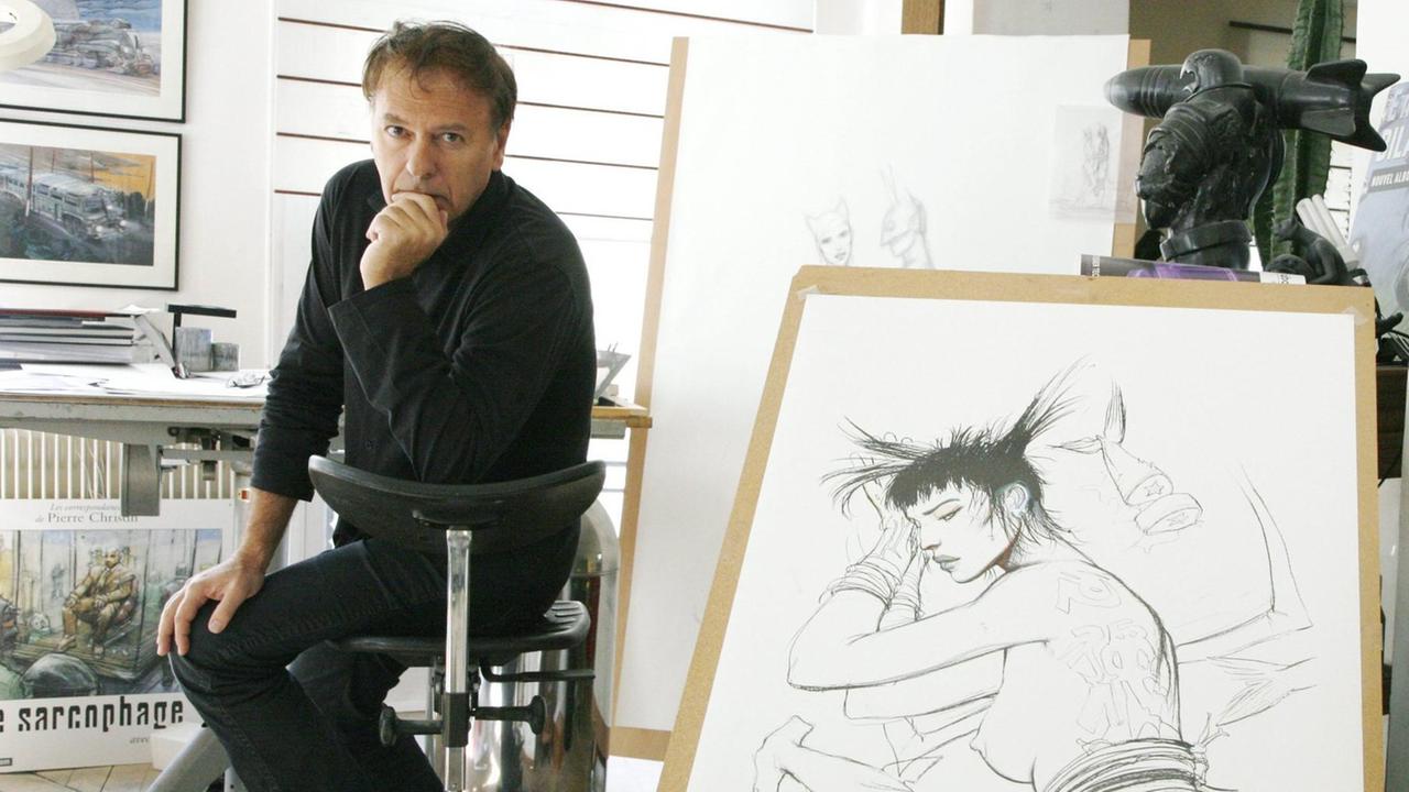 Enki Bilal blickt nachdenklich in die Kamera, neben ihm steht das gezeichnete Bild einer schlafenden Frau. Enki Bilal blickt nachdenklich in die Kamera, neben ihm steht das gezeichnete Bild einer schlafenden Frau.