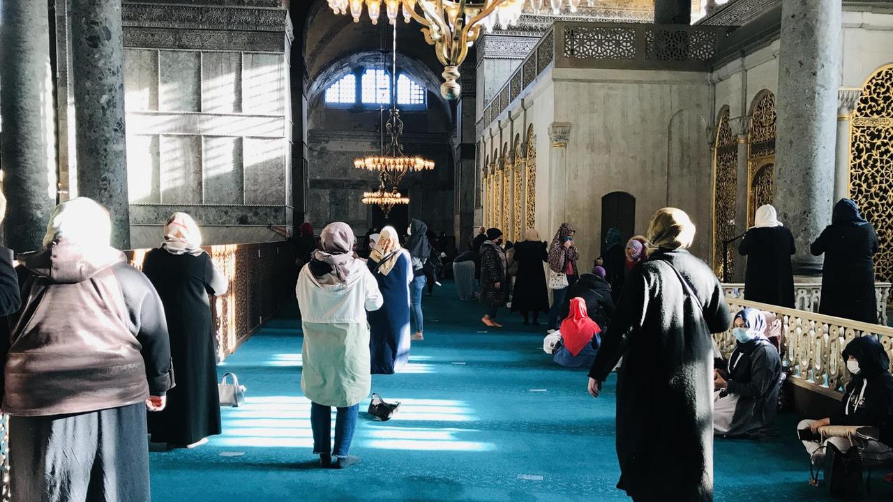Mehrere Frauen mit bedecktem Kopf laufen über den türkisgrünen Teppich in der Hagia Sophia.