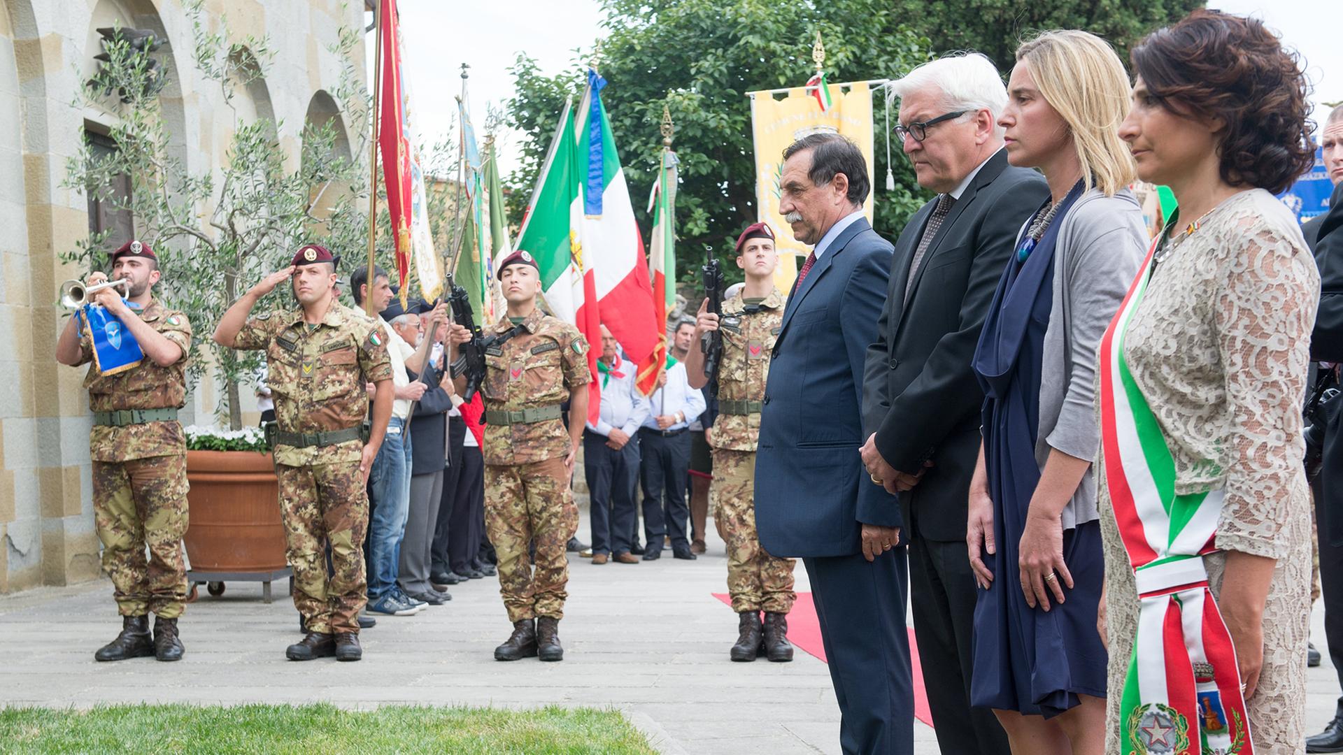 Steinmeier, Mogherini und Minchetti stehen an einem Grab, im Hintergrund salutieren Soldaten.