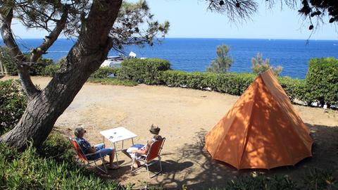 Camper sitzen an einem Tisch neben ihrem Zelt mit Blick auf den See auf einem Zeltplatz in Argeles-sur-mer in Südfrankreich.