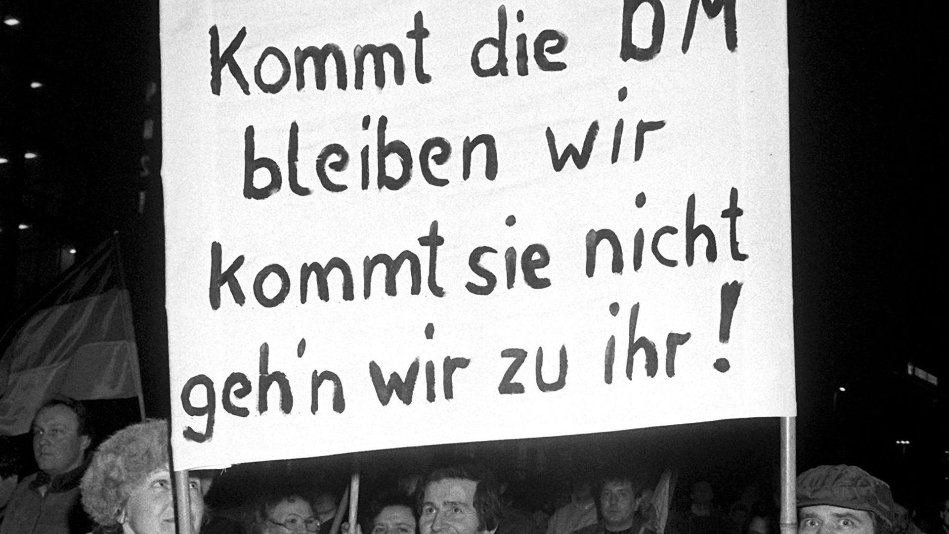 "Kommt die DM bleiben wir kommt sie nicht geh'n wir zu ihr!" ist auf einem Transparent zu lesen, das ein Paar bei einer Montagsdemonstration am 12.2.1990 in Leipzig mit sich führt. Die von den Demonstranten hier geforderte Einführung der D-Mark in der DDR wurde im Rahmen der per Staatsvertrag vereinbarten Wirtschafts-, Währungs- und Sozialunion am 1.7.1990 realisiert. Sie bildete einen entscheidenden Schritt zur Wiedervereinigung der beiden deutsche Staaten am 3.10.1990. "Kommt die DM bleiben wir kommt sie nicht geh'n wir zu ihr!" ist auf einem Transparent zu lesen, das ein Paar bei einer Montagsdemonstration am 12.2.1990 in Leipzig mit sich führt. Die von den Demonstranten hier geforderte Einführung der D-Mark in der DDR wurde im Rahmen der per Staatsvertrag vereinbarten Wirtschafts-, Währungs- und Sozialunion am 1.7.1990 realisiert. Sie bildete einen entscheidenden Schritt zur Wiedervereinigung der beiden deutsche Staaten am 3.10.1990.