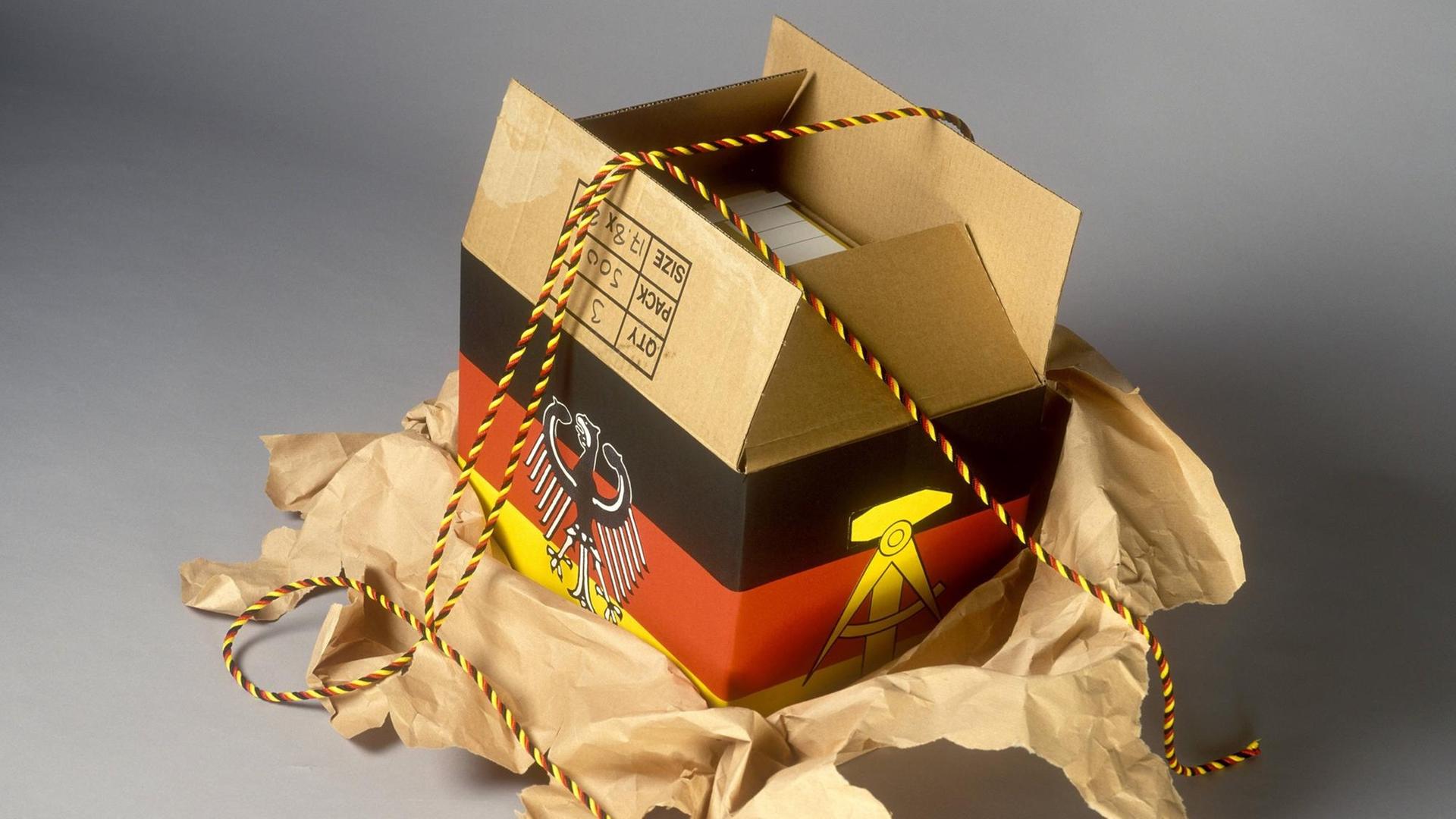Ein geöffnetes schwarz-rot-goldenes Paket mit den Symbolen der BRD und DDR. Ein geöffnetes schwarz-rot-goldenes Paket mit den Symbolen der BRD und DDR.