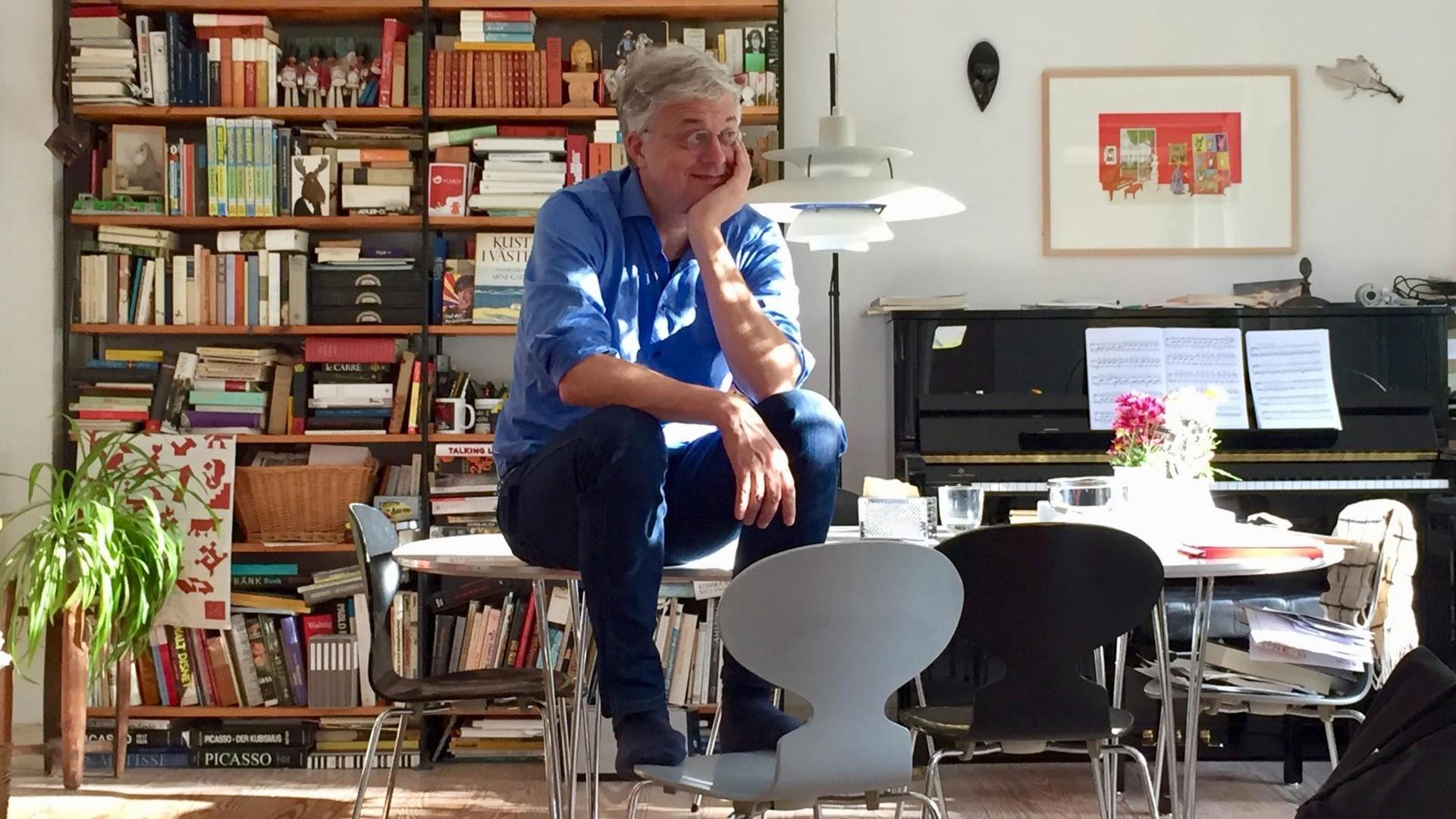 Ole Könnecke sitzt auf einem Tisch, im Hintergrund Bücherregal und Klavier