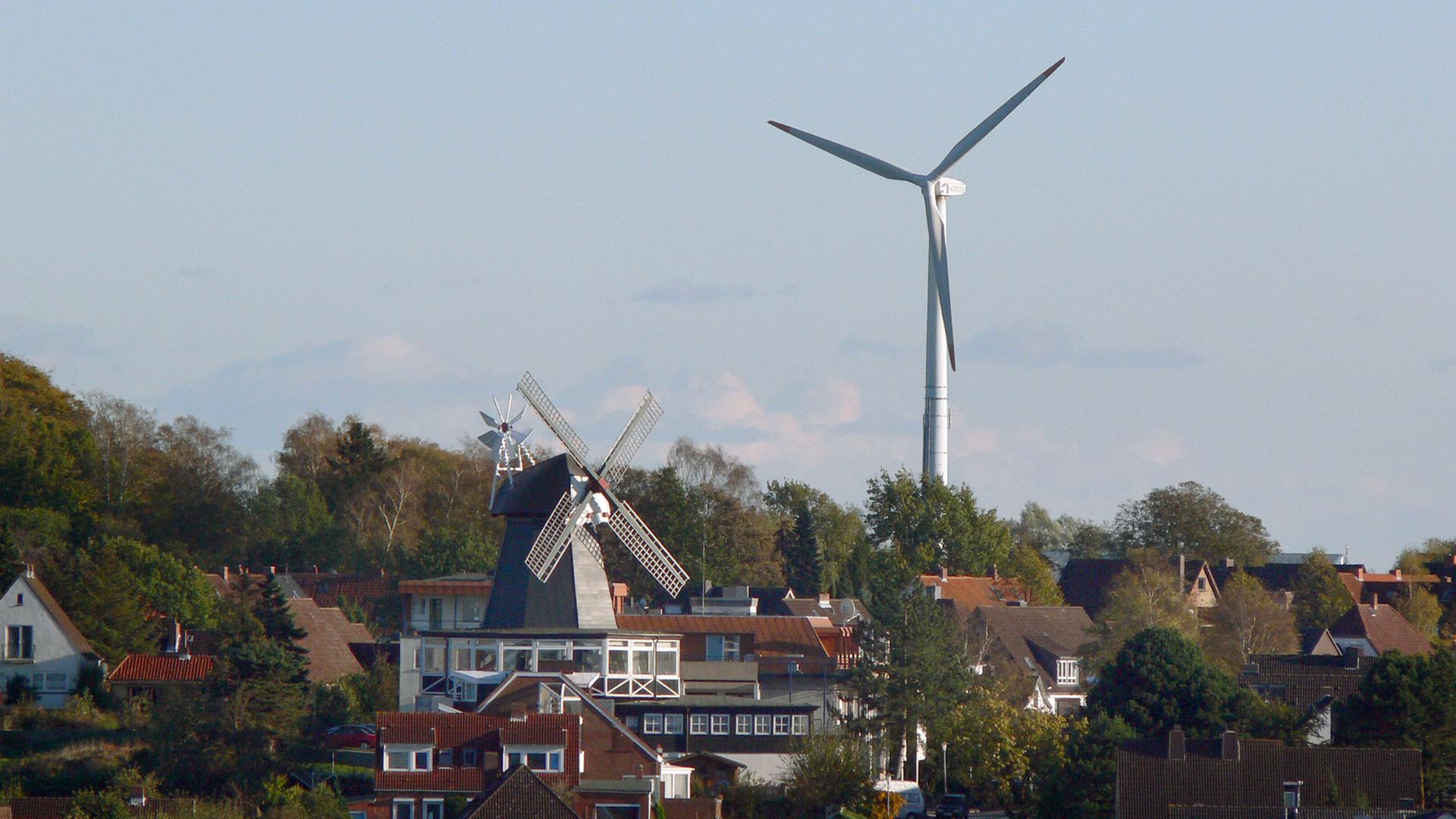 Eine alte Windmühle steht zwischen Wohnhäusern in Kiel, im Hintergrund ein modernes Windrad. Eine alte Windmühle steht zwischen Wohnhäusern in Kiel, im Hintergrund ein modernes Windrad.