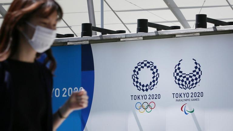 Eine Japanerin mit Mundschutz läuft an den Loos der Olympischen und Paralympischen Spielen in Tokio vorbei